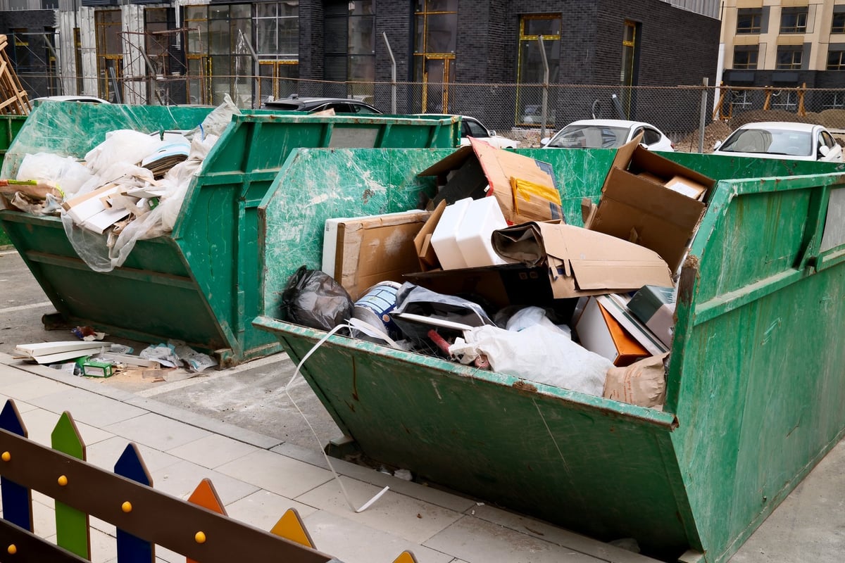 Overflowing green construction dumpster filled with cardboard boxes and building waste