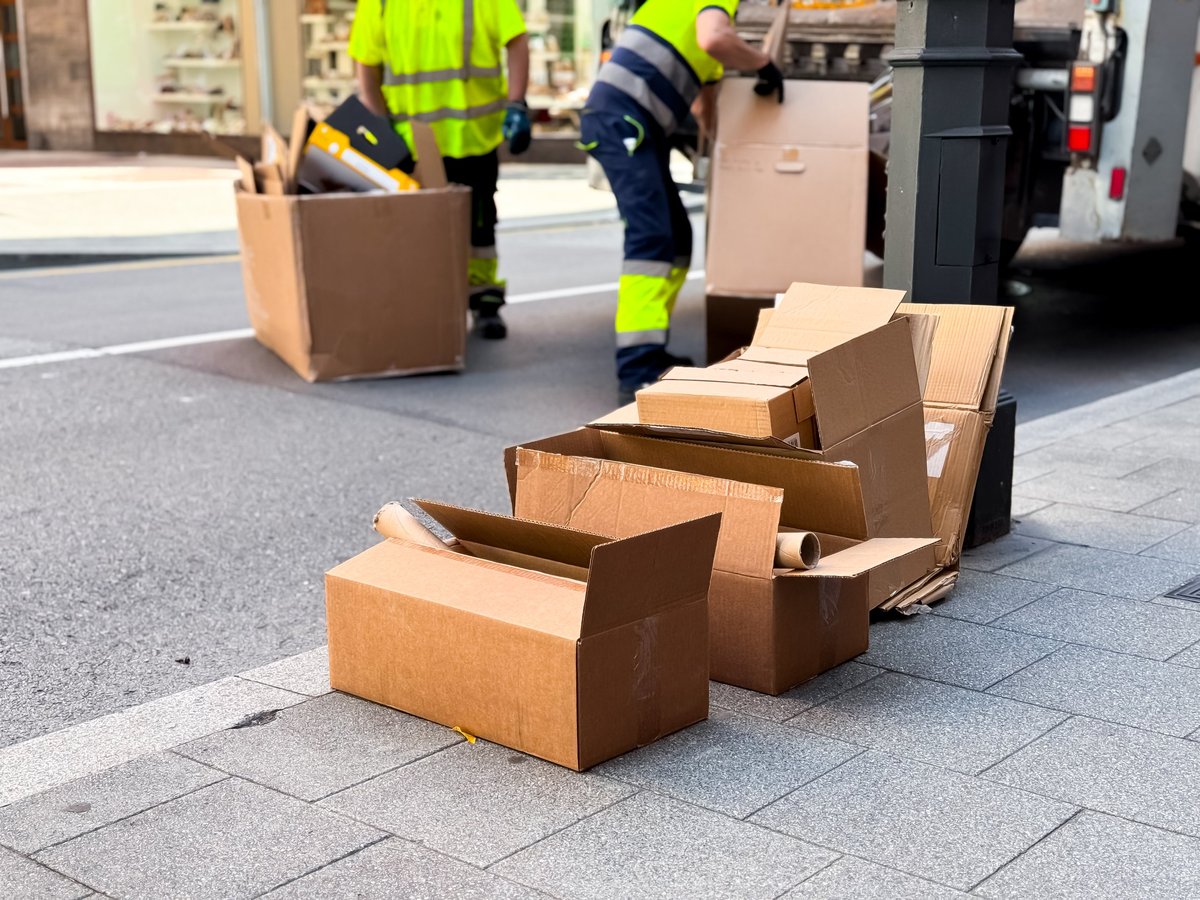 Workers dispose of cardboard boxes on city street sidewalk