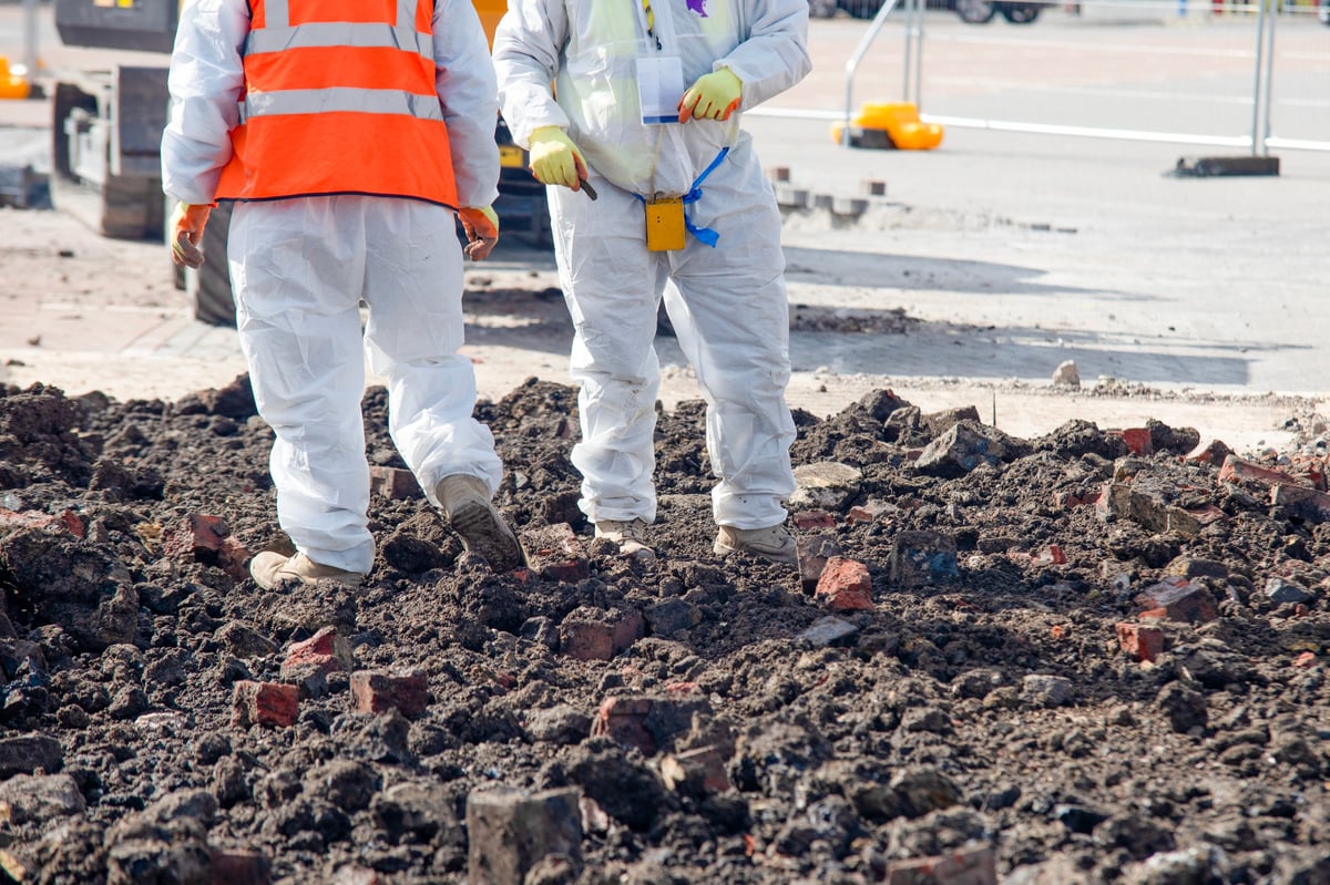 Two construction workers in safety gear inspect a construction site covered with broken soil and bricks