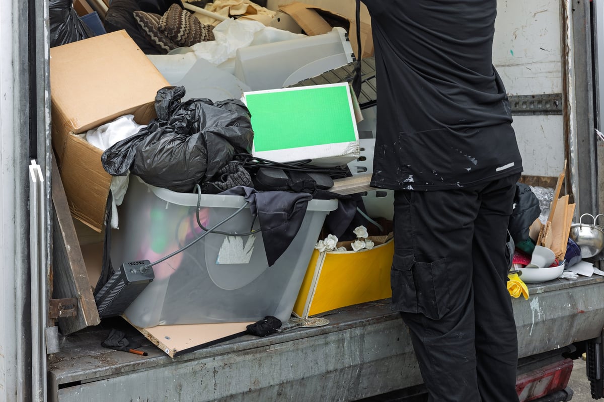 Worker unloading mixed waste, household items, and rubbish from the rear of a commercial truck