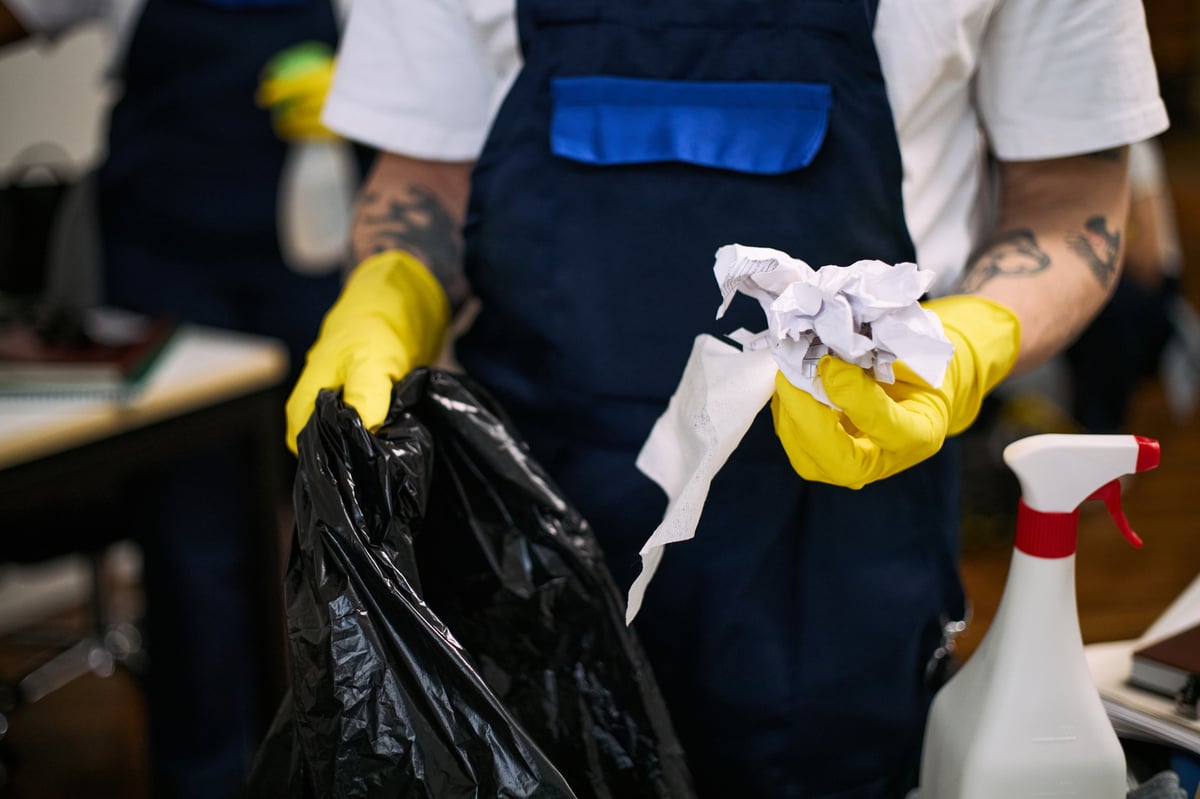 Young adult Caucasian man wearing yellow gloves cleaning office workspace