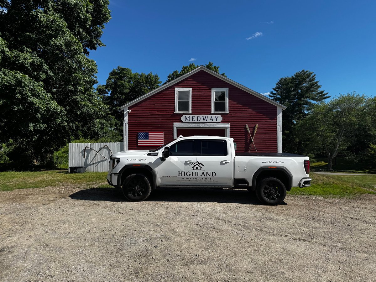 White GMC truck parked in front of a red barn with American flag under blue sky